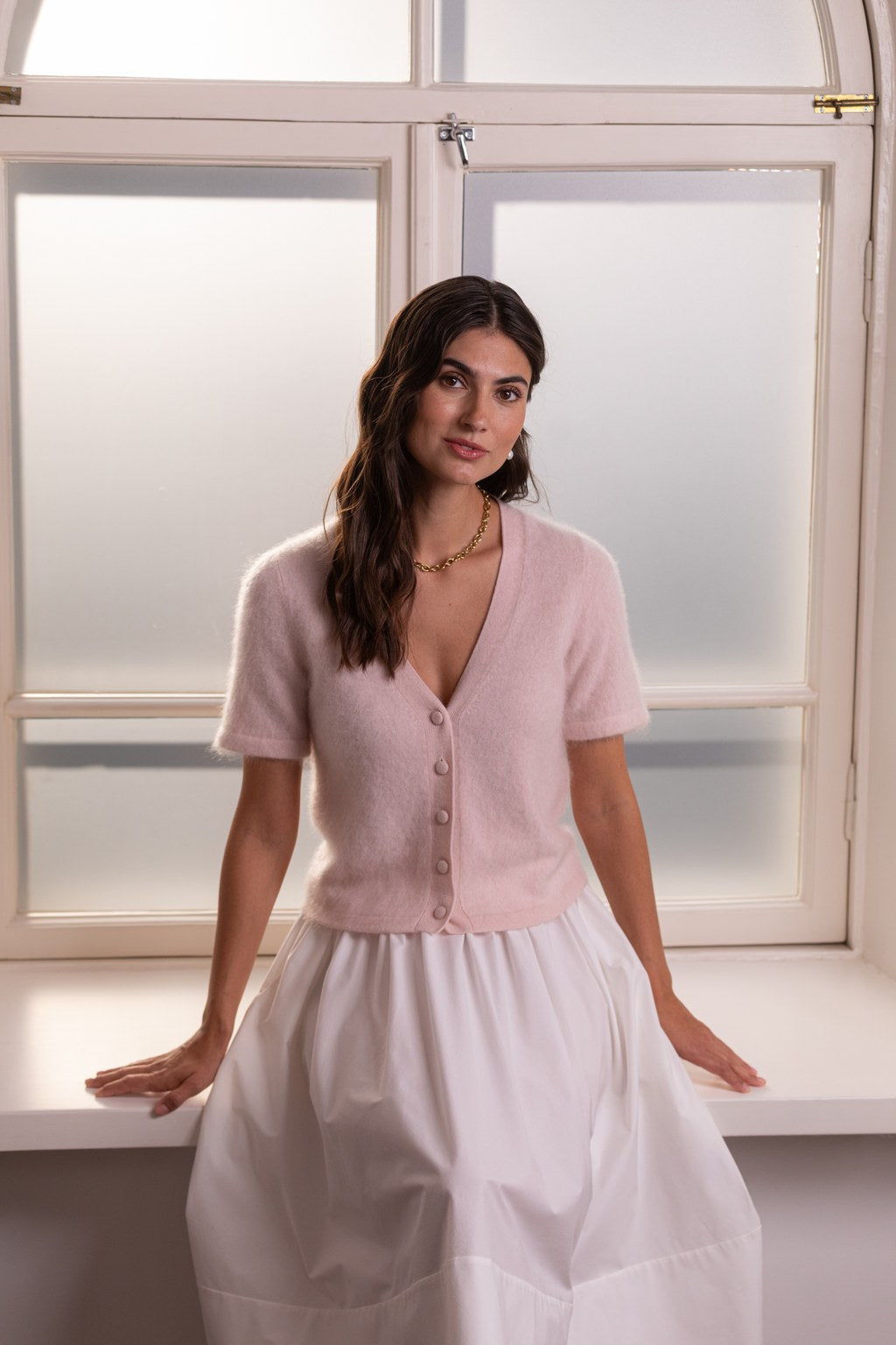 Nainen, jonka päällä on Original Storyn lyhythihainen v-kaula-aukollinen kashmirneuletakki sekä valkoinen puuvillahame